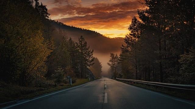 Carretera recta hacia el horizonte en una puesta de sol tras la montaña.